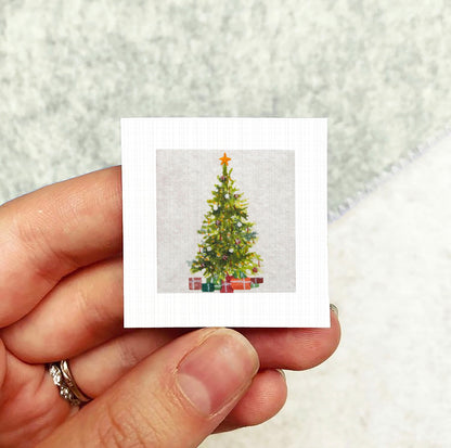 A hand holding a small square card with a picture of a Christmas tree on it.