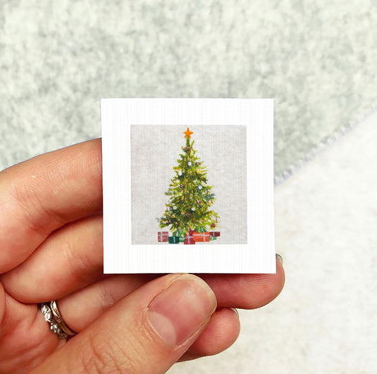 A hand holding a small square card with a picture of a Christmas tree on it.
