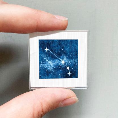 A person's hand holding a small square-shaped object with a picture of a starry night sky on it.