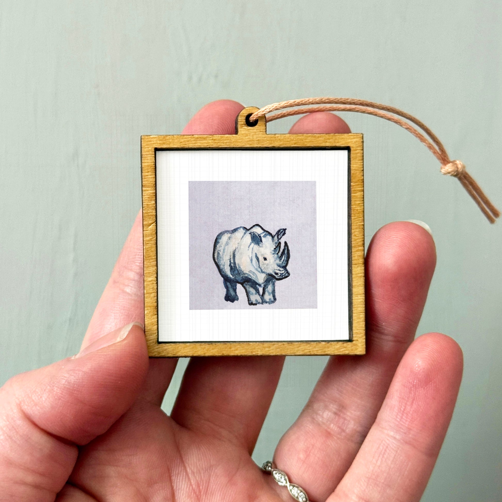 A person's hand holding a small wooden frame containing a picture of a rhinoceros.