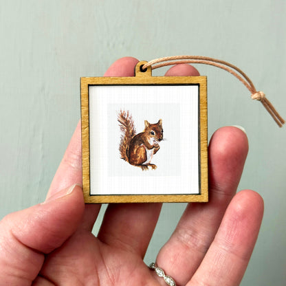 A person's hand holding a small wooden frame containing a picture of a squirrel.