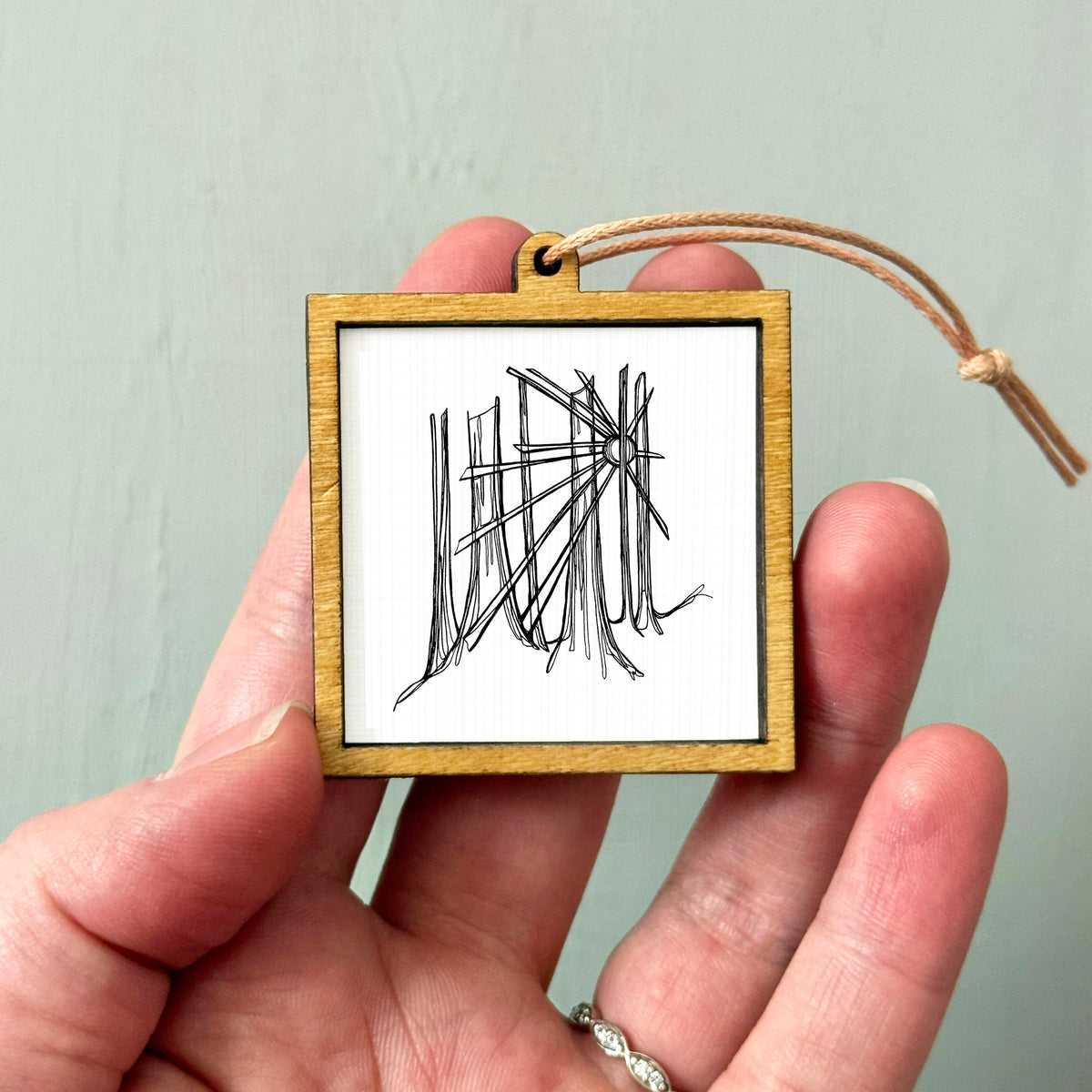 A hand holding a small wooden frame with a black and white abstract drawing inside it.