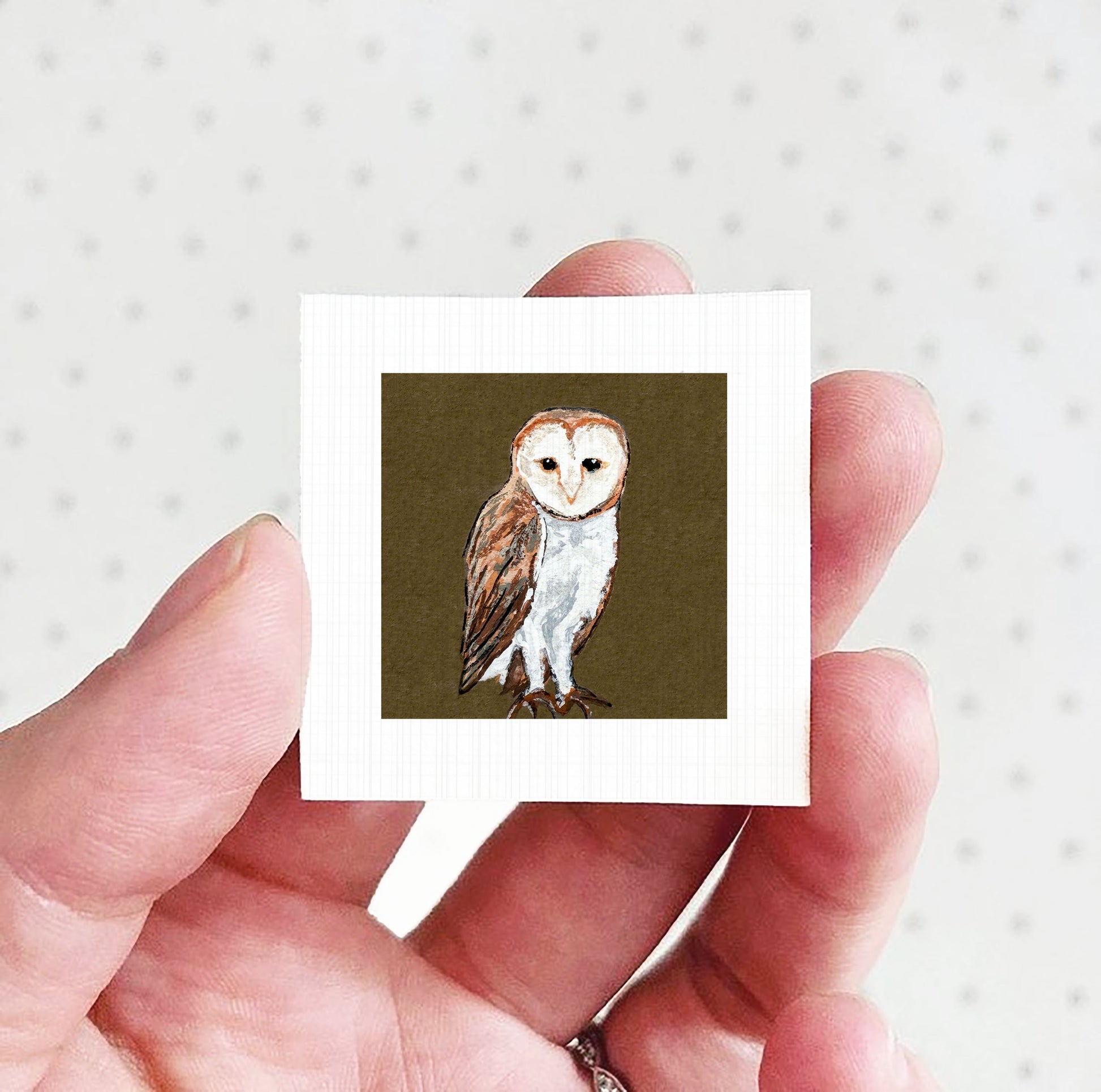 A hand holding a small square picture of an owl against a white background.