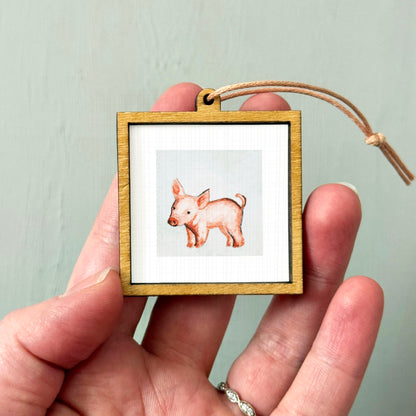 A hand holding a small wooden frame containing a picture of a pig.