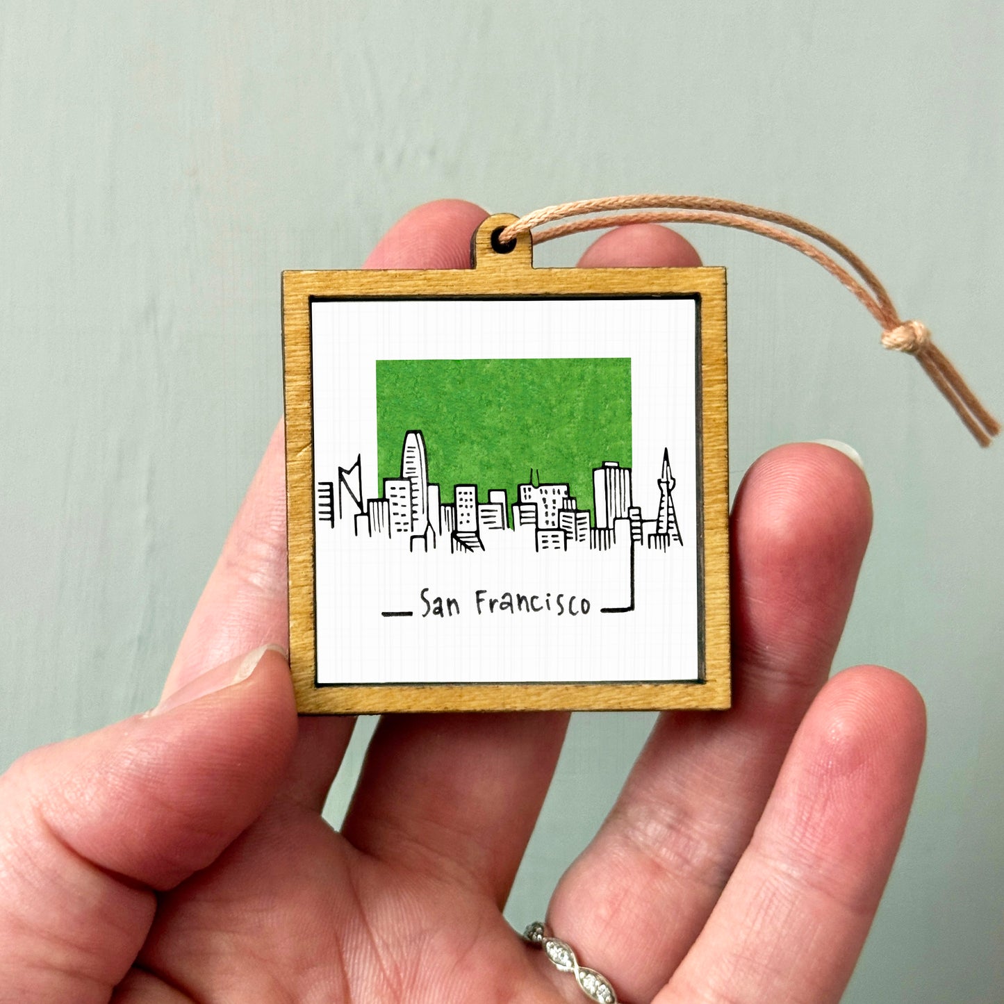 A hand holding a small wooden frame with a picture of a city skyline and the text "San Francisco" written below it.
