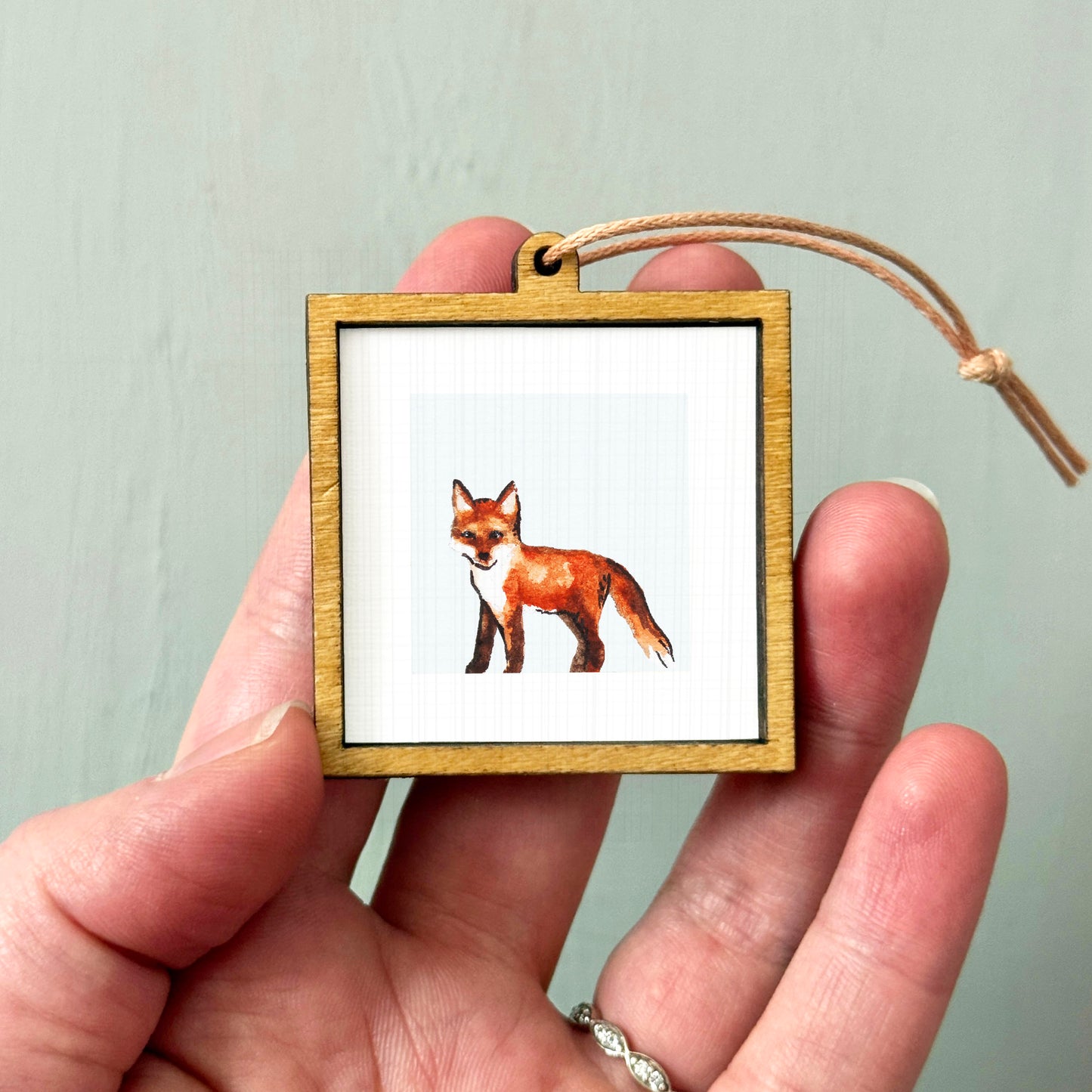 A person's hand holding a small wooden frame containing a picture of a fox.