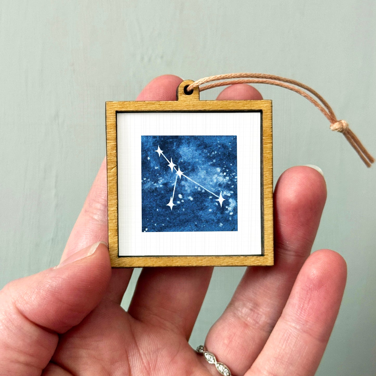 A hand holding a small wooden frame containing a framed image of a starry night sky.