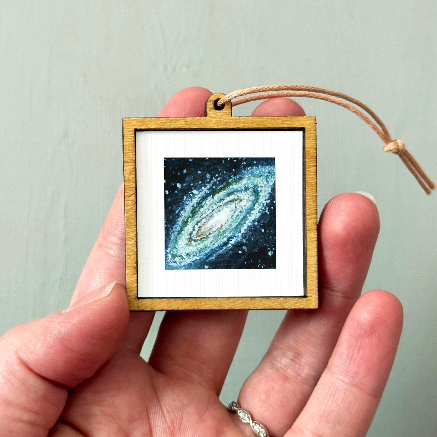 A hand holding a small wooden frame containing a framed image of a galaxy.