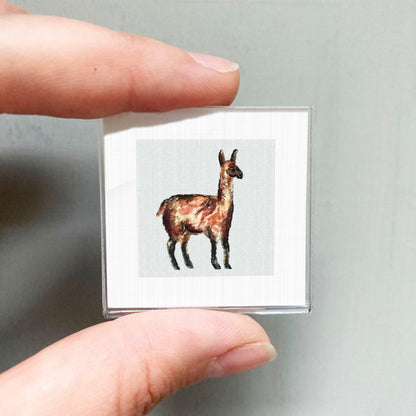 A person's hand holding a small square picture of a llama.