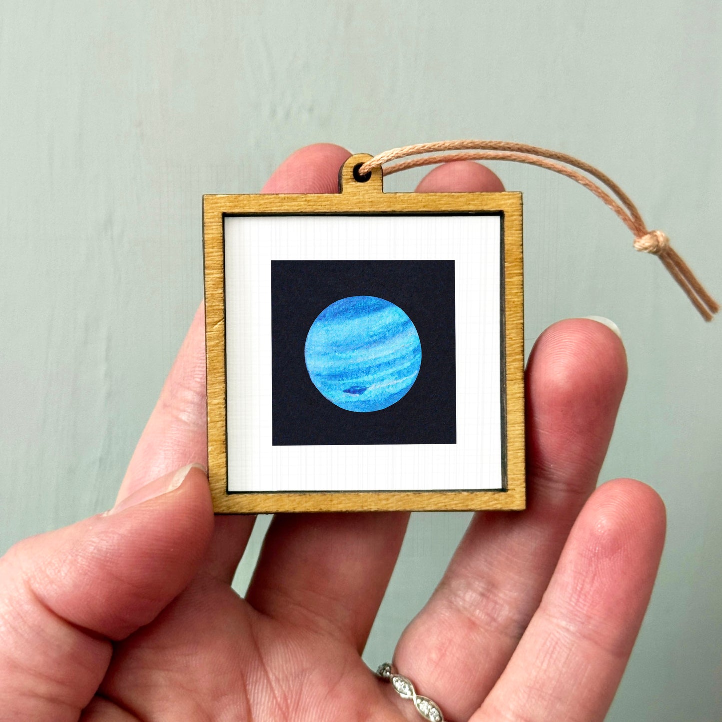 A hand holding a small wooden frame containing a picture of the planet Neptune.