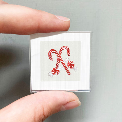 A person's hand holding a small square picture of two red and white striped candy canes.