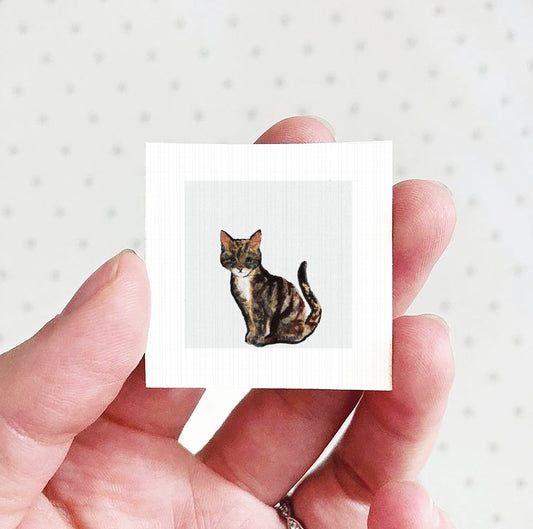 A hand holding a small square picture of a cat.