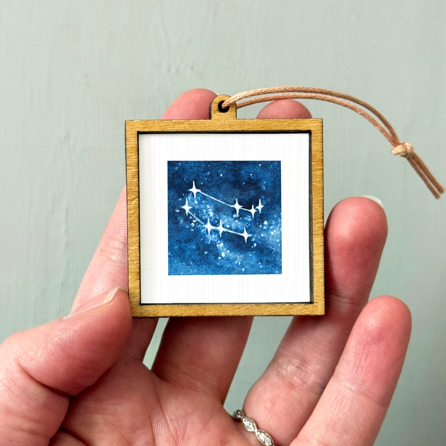 A hand holding a small wooden frame containing a framed image of a starry night sky.