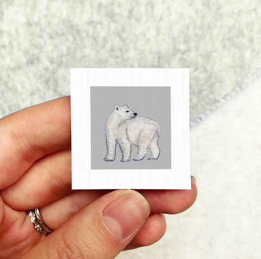 A person's hand holding a small square card with an image of a polar bear on it.