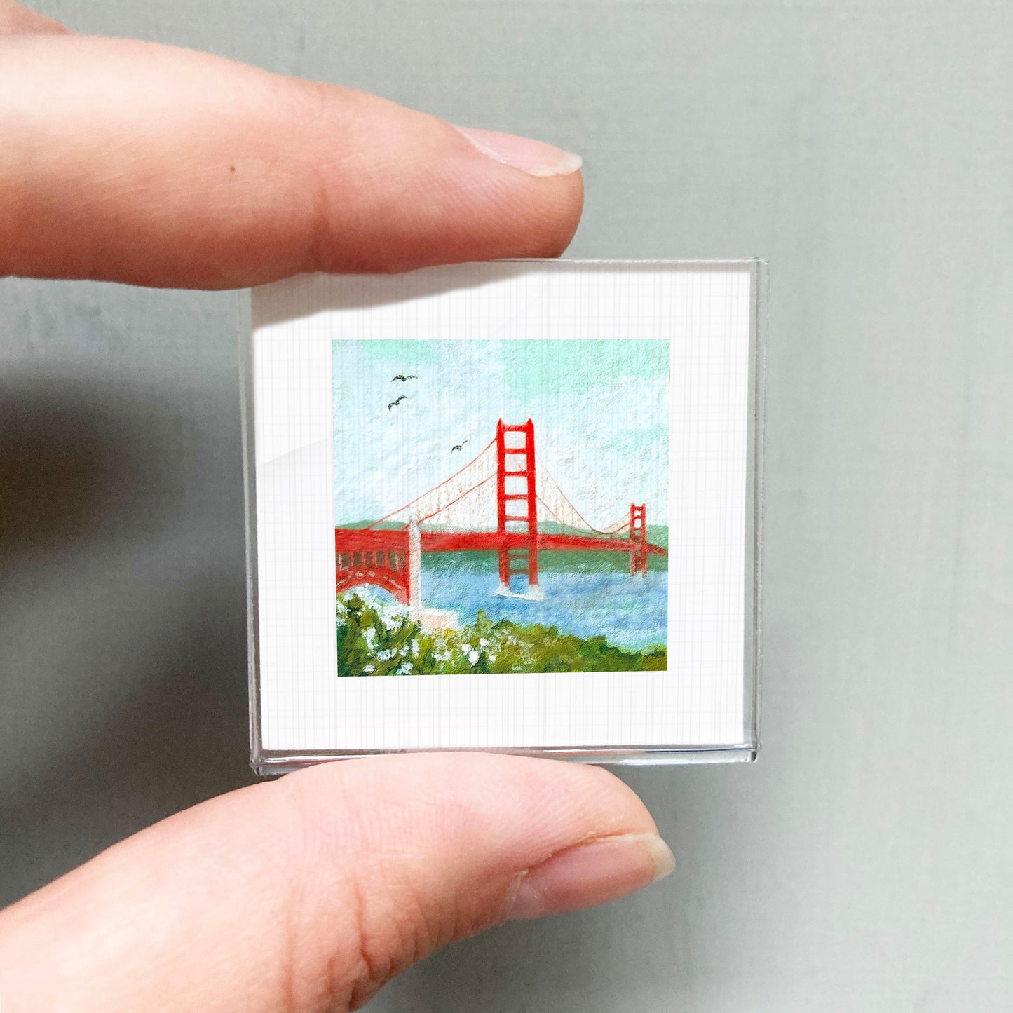 A person's hand holding a small square picture of the Golden Gate Bridge.