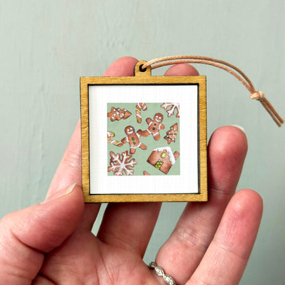 A hand holding a small wooden frame containing a picture of gingerbread men and snowflakes.