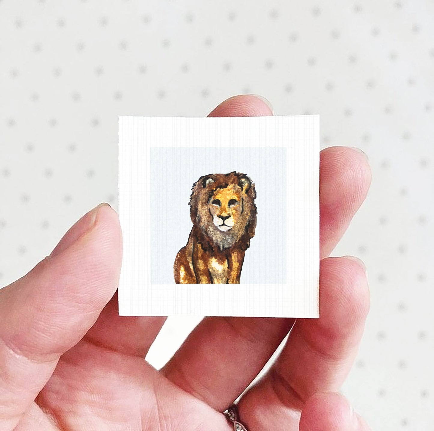 A hand holding a small square picture of a lion.