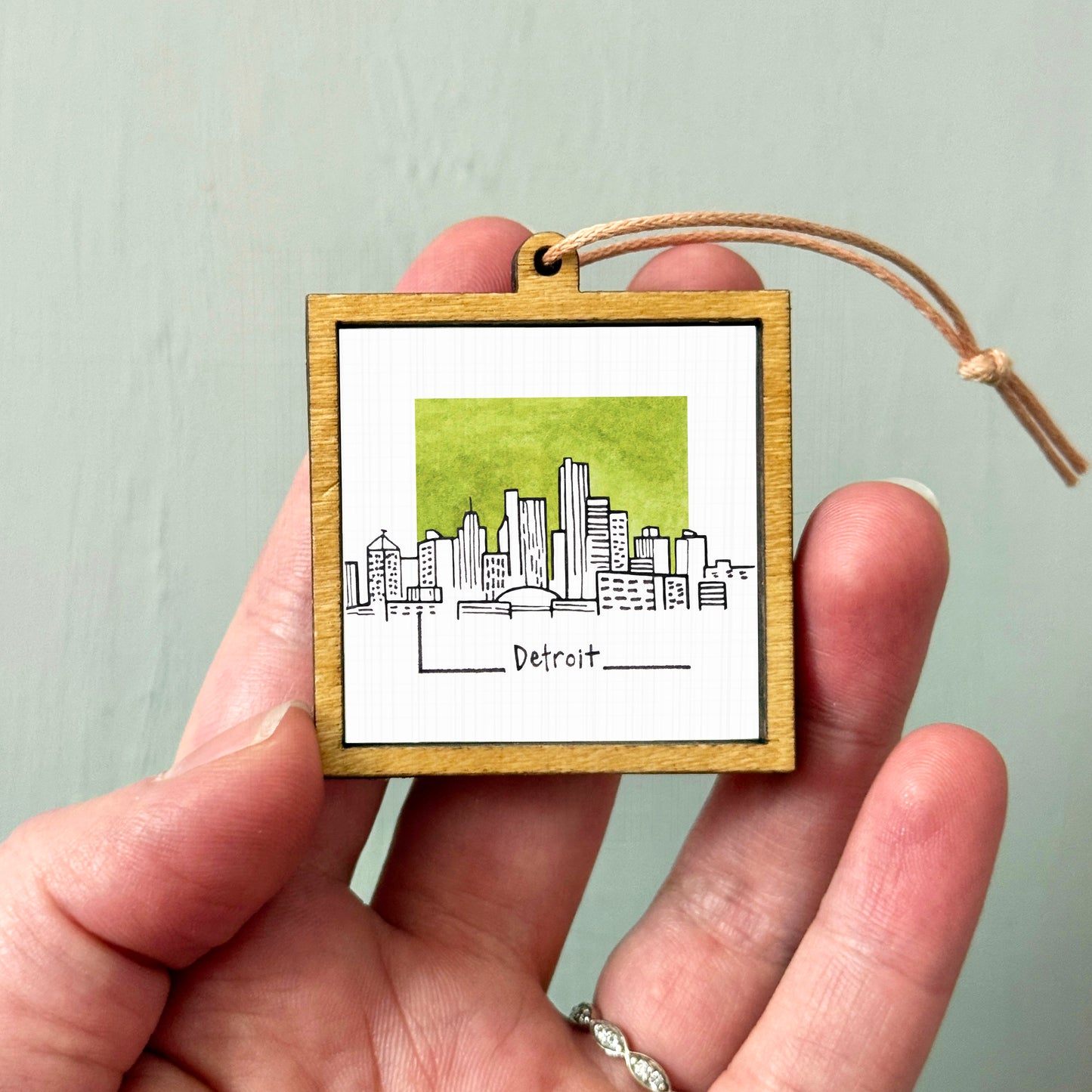 A hand holding a small wooden frame with a picture of a city skyline, specifically Detroit, inside it.