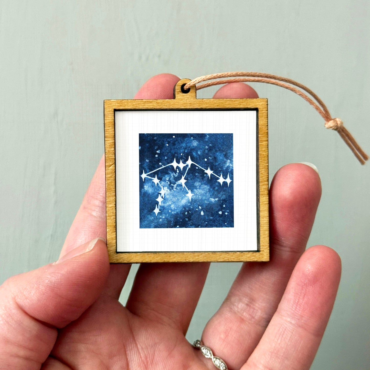 A hand holding a small wooden frame containing a framed image of a starry night sky.