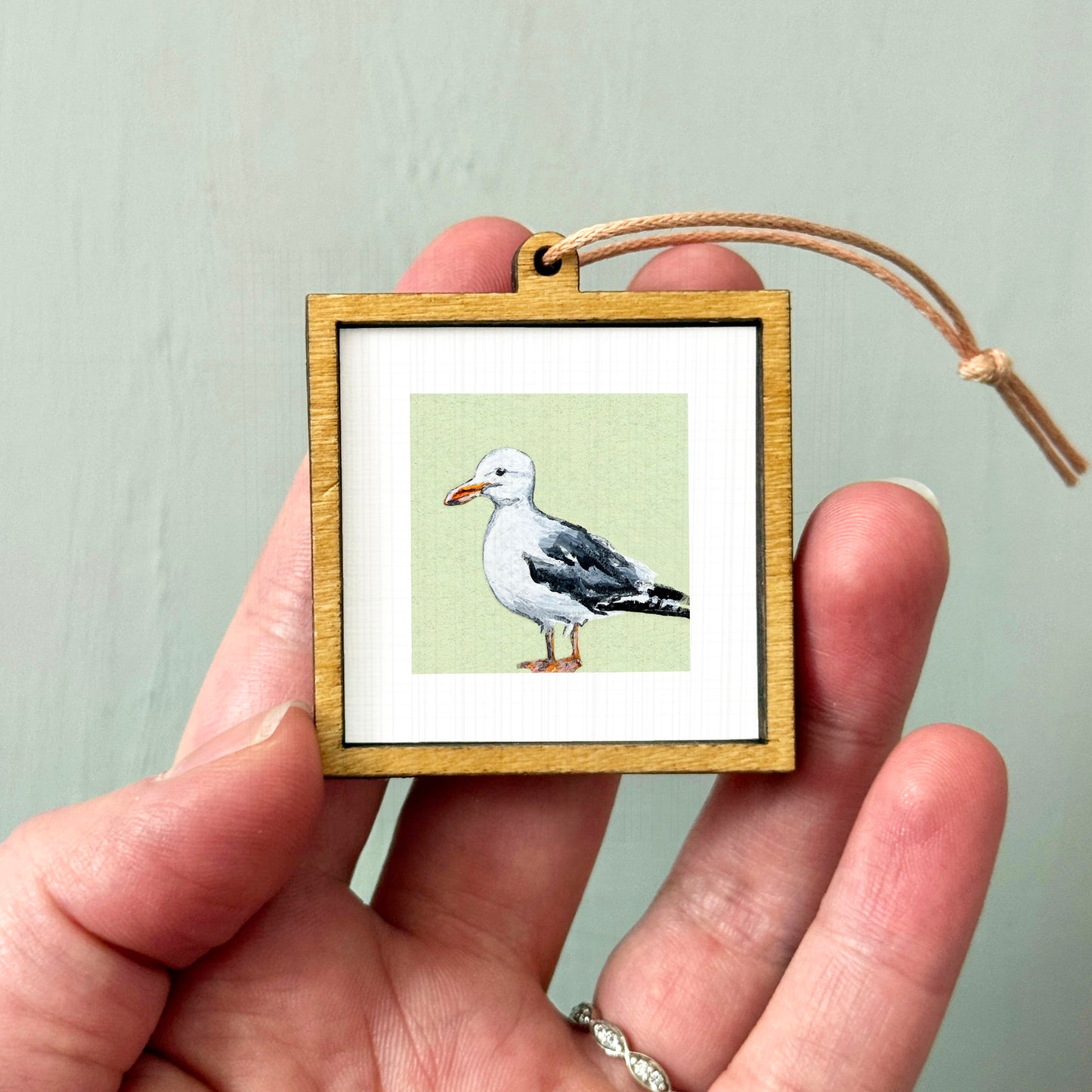 A person's hand holding a small wooden frame containing a framed image of a seagull.