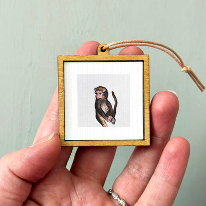 A person's hand holding a small wooden frame containing a picture of a monkey.