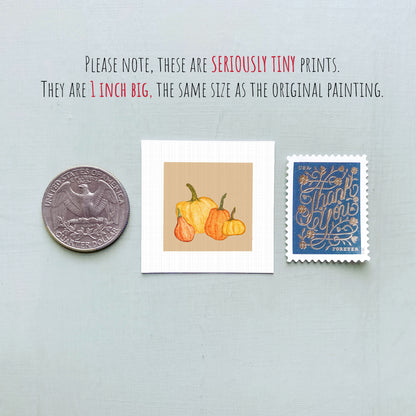 three small prints: a United States quarter, a square print of pumpkins, and a blue postage stamp with gold lettering.