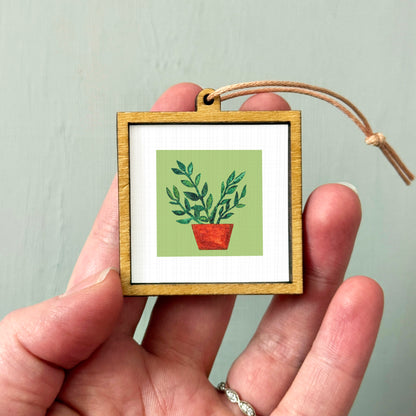 A hand holding a small wooden frame containing a picture of a potted plant.