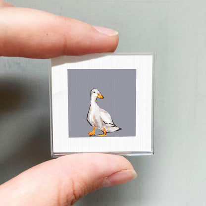 A person's hand is holding a small square picture of a duck against a gray background.