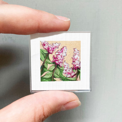 A person's hand holding a small square picture of pink flowers against a white background.