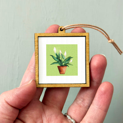 A person's hand holding a small wooden frame containing a picture of a potted plant.