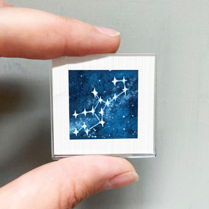 A hand is holding a small square-shaped object with a blue starry night sky image on it.