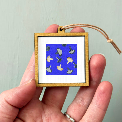 A hand holding a small wooden frame containing a picture of mushrooms against a blue background.