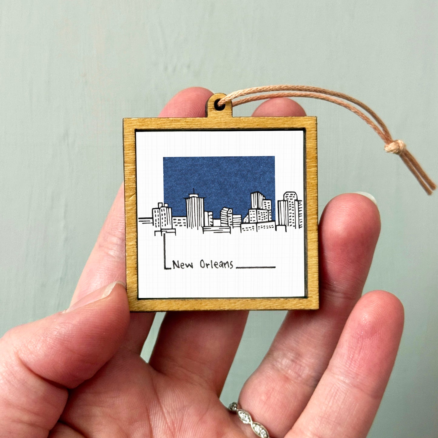A hand holding a small wooden frame with a picture of the skyline of New Orleans.