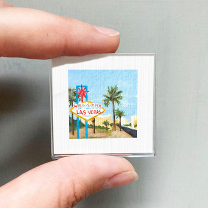 A person's hand holding a small framed picture of the famous Las Vegas sign.