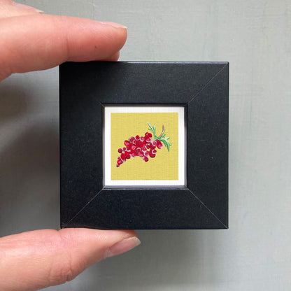 A person's hand holding a small black frame containing a vibrant yellow square with a red flower design.