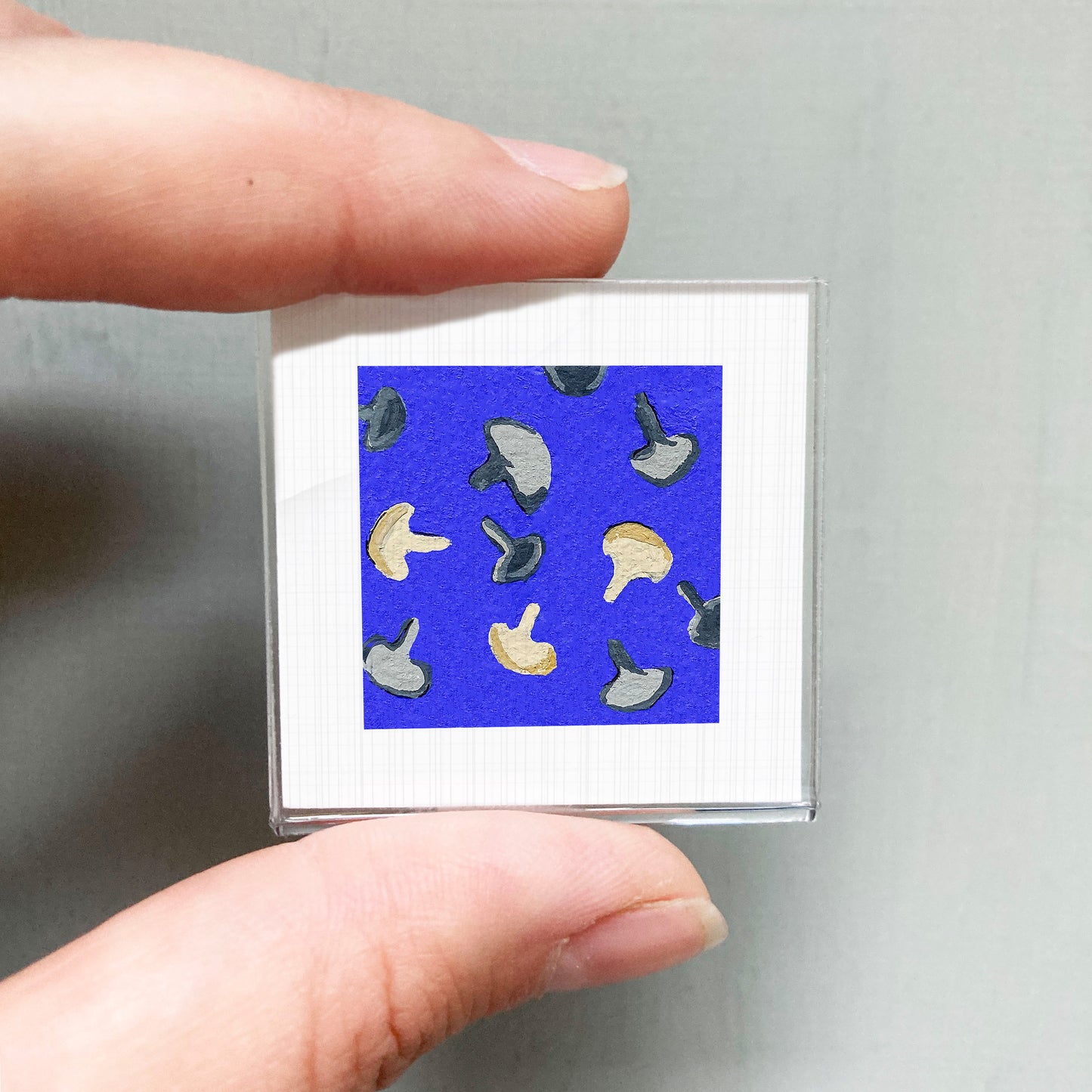 A person's hand is holding a small square with a blue background and a pattern of mushrooms on it.