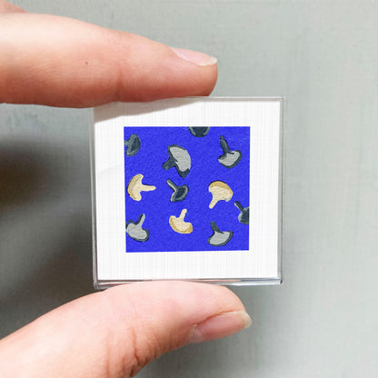 A person's hand is holding a small square with a blue background and a pattern of mushrooms on it.