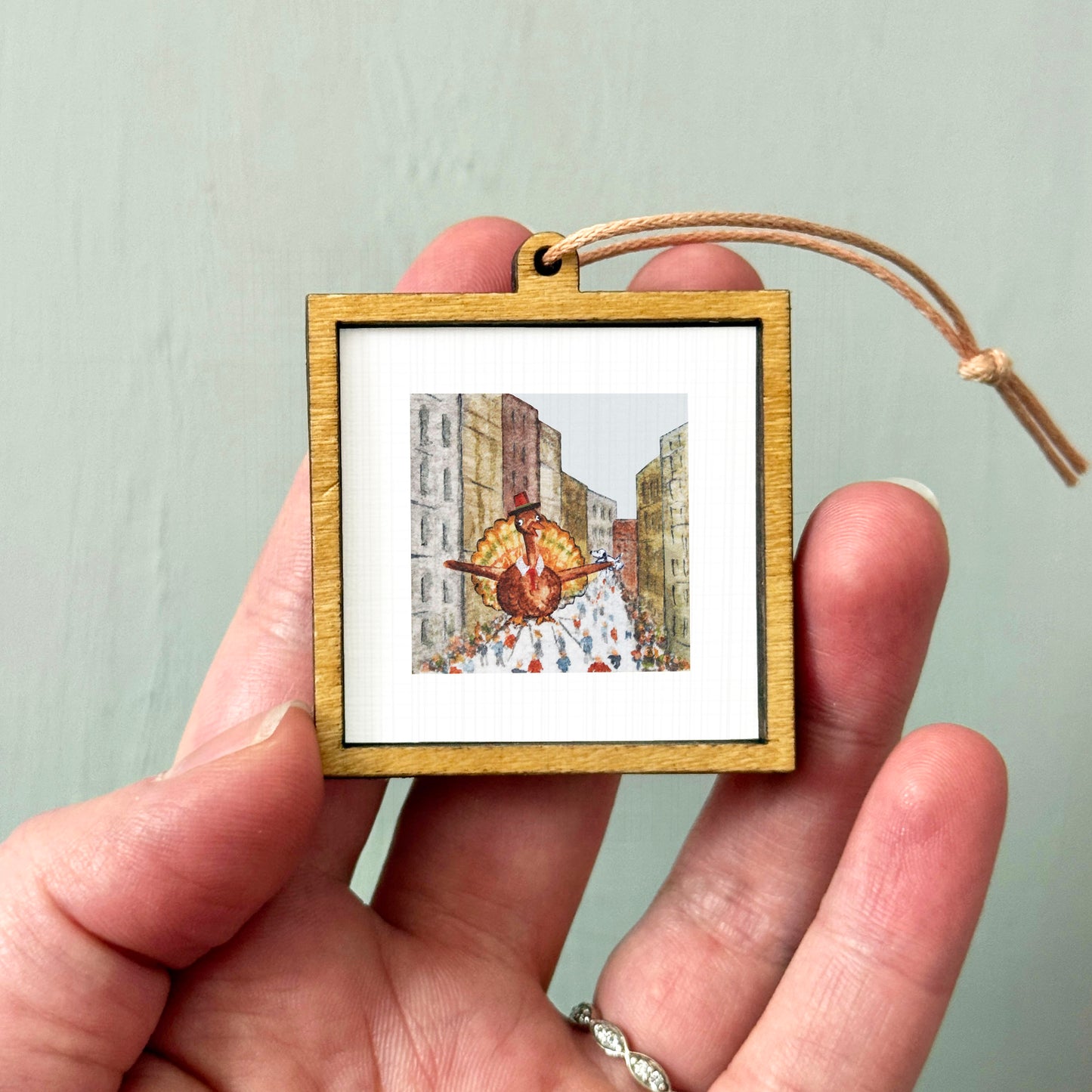 A person's hand is holding a small wooden frame containing a framed illustration of a person walking down a city street.