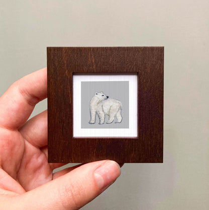 A hand is holding a small wooden frame containing a picture of a polar bear.