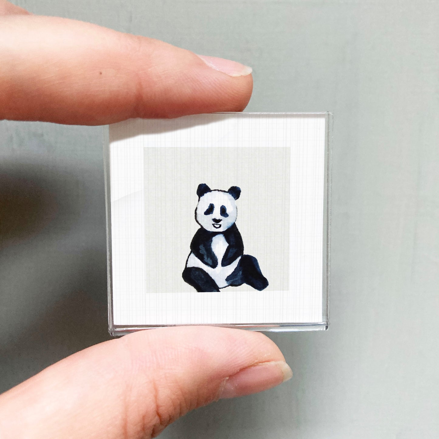 A person's hand holding a small square with a panda bear image on it.