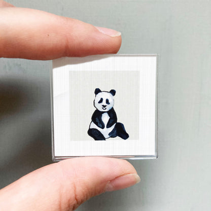 A person's hand holding a small square with a panda bear image on it.