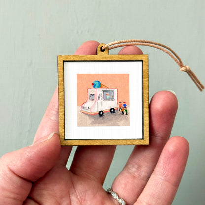 A person's hand is holding a small wooden frame containing a picture of an ice cream truck.
