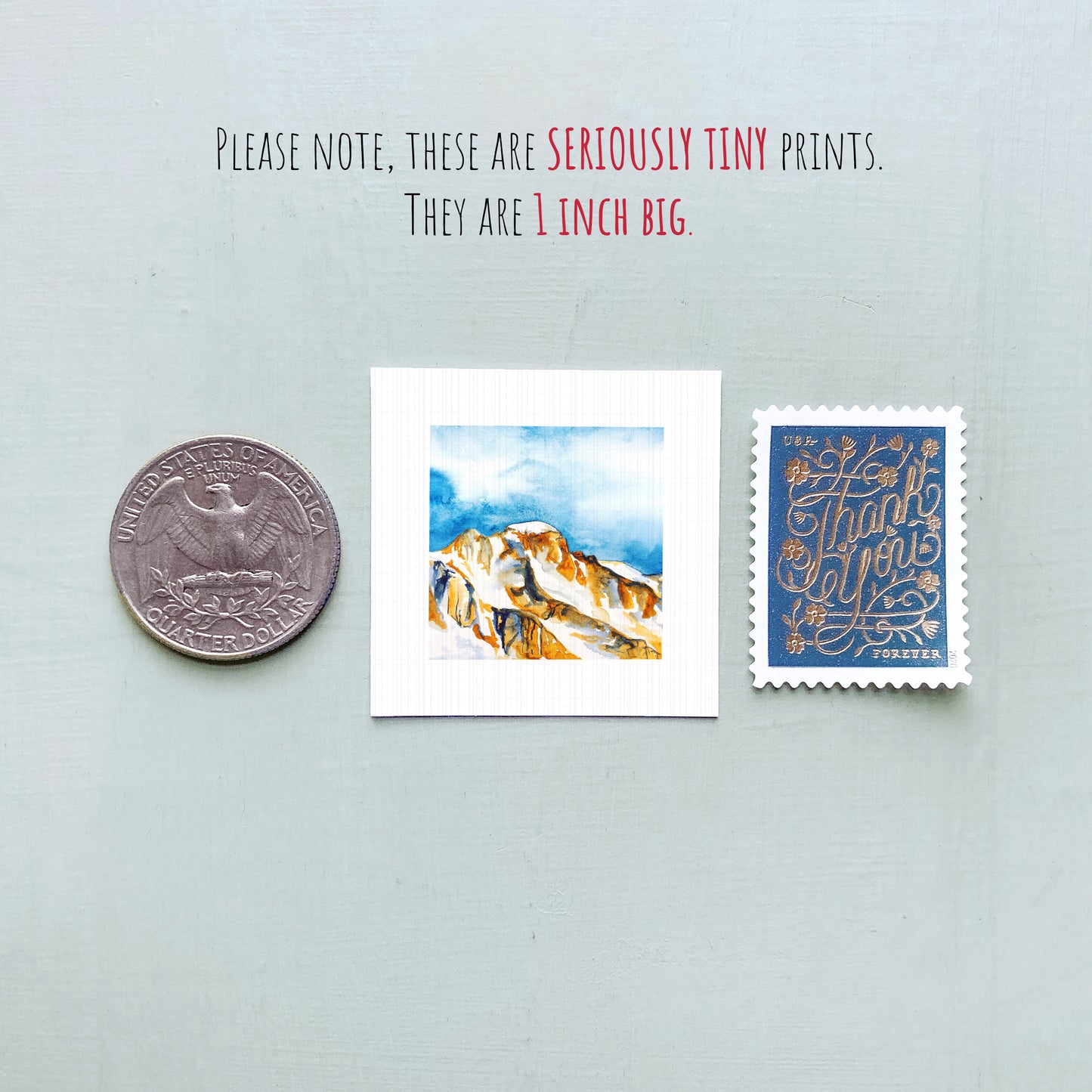 a collection of three small items: a quarter, a watercolor painting of a mountain, and a postage stamp.