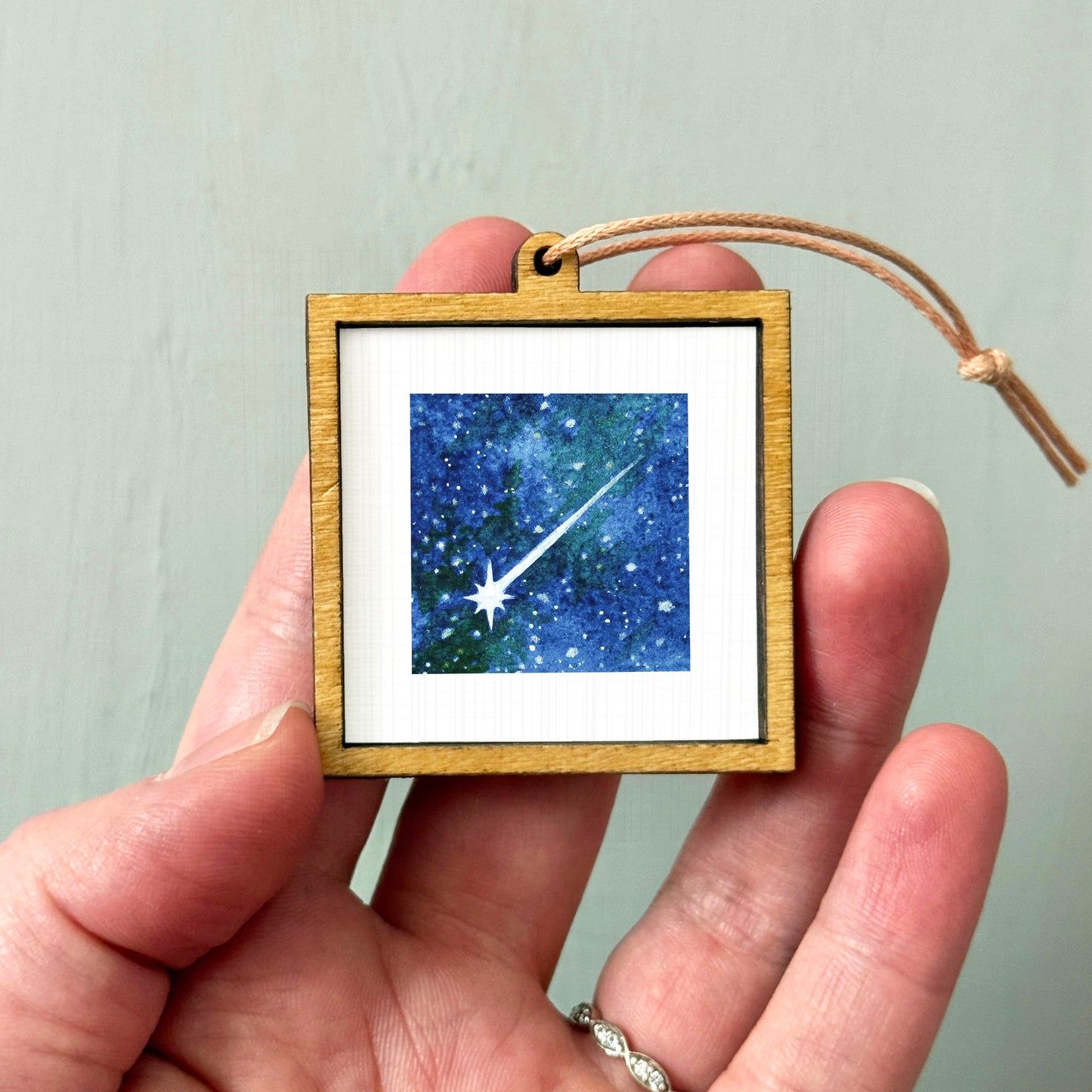 A hand holding a small wooden frame containing a picture of a starry night sky.