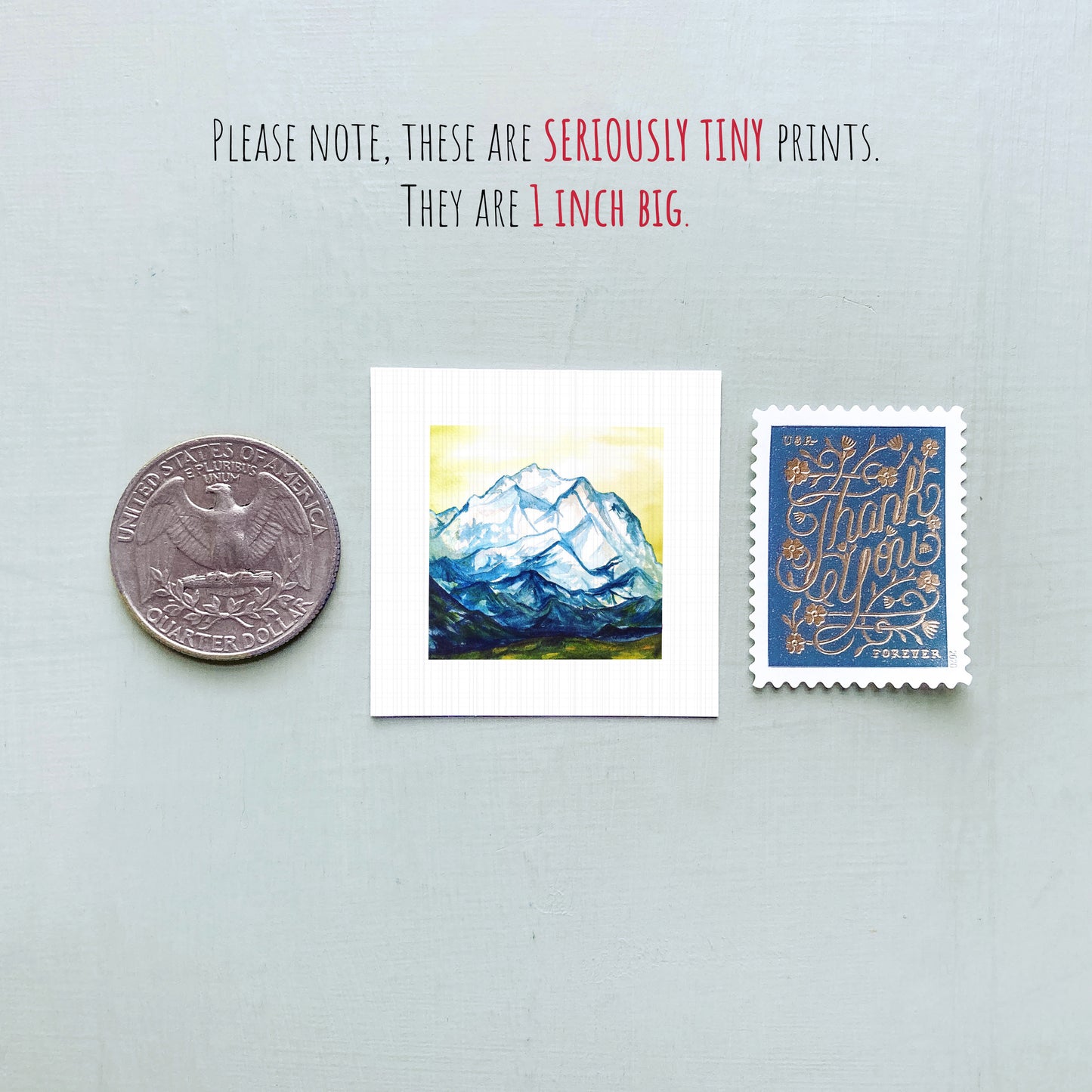 three tiny prints: a United States quarter, a small square print with a mountain landscape, and a blue postage stamp with gold lettering.
