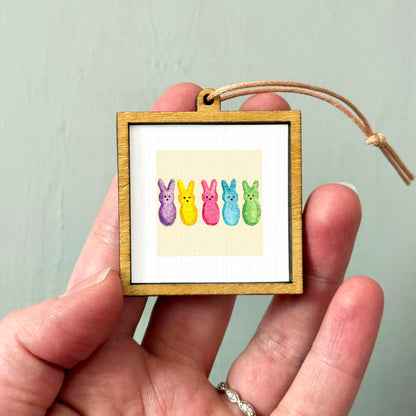 A hand holding a small wooden frame containing a picture of five colorful Easter bunny characters.