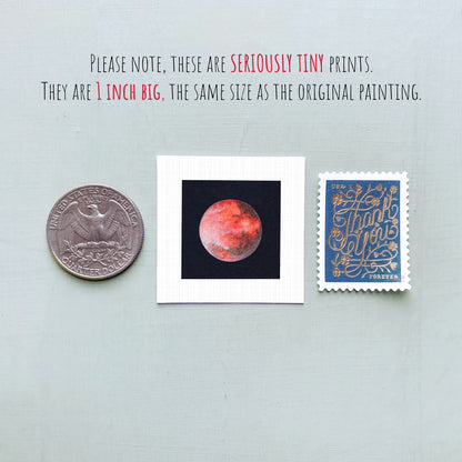 three small prints: a silver coin, a white square print of a red planet, and a blue postage stamp with gold lettering.