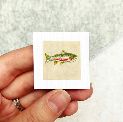 A person's hand holding a small square card with a colorful illustration of a fish on it.