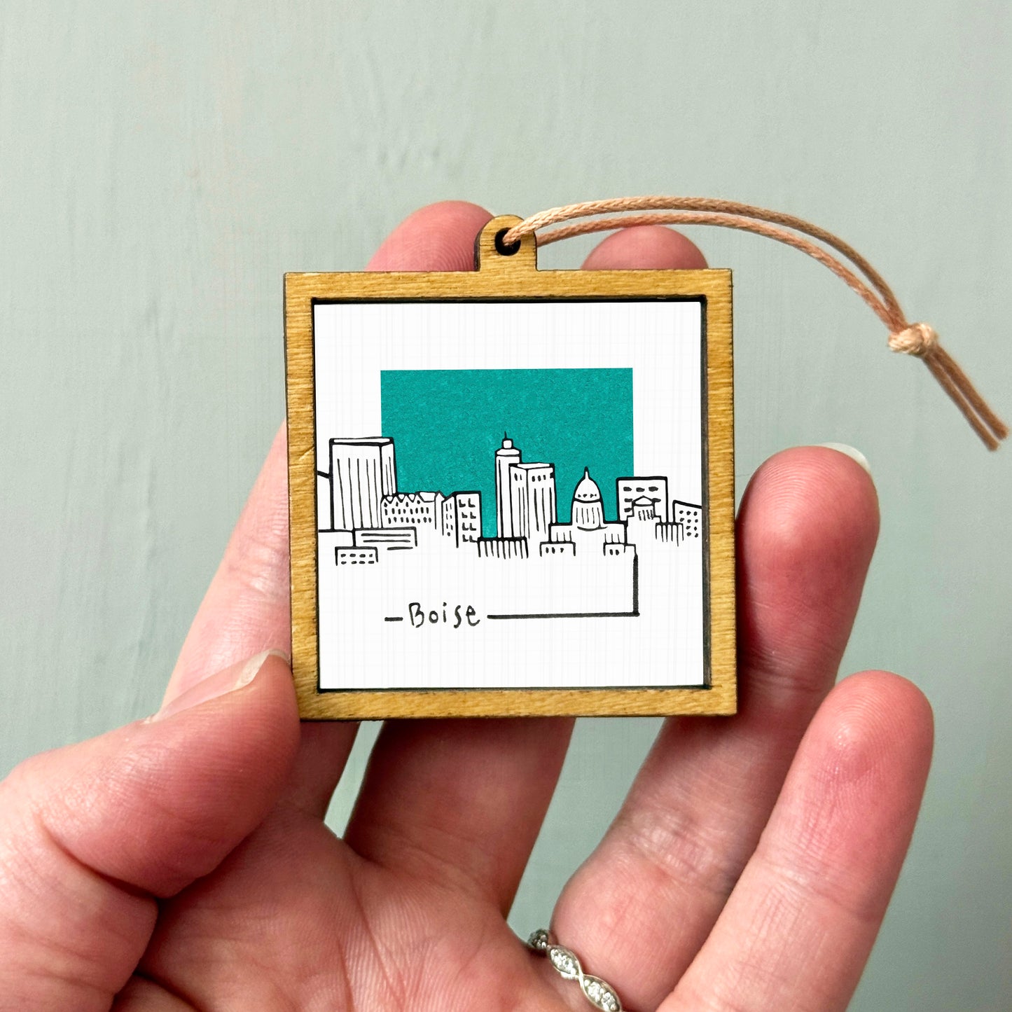 A hand holding a small wooden frame with a picture of a city skyline on it.