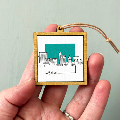 A hand holding a small wooden frame with a picture of a city skyline on it.